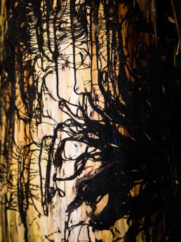 Rest of plants embrace a tree trunk, their black fibers trace lines like a painting on a golden trunk.